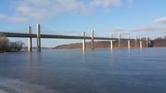 a large bridge over a frozen river with trees on both sides and hills in the background