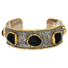 Elevate your style with this luxurious cuff bracelet, a stunning masterpiece designed by the renowned Victor Velyan. This exquisite piece features five striking black tourmalines, set in a captivating blend of 24K gold. The black tourmalines, with their deep, mysterious allure, are gemstones known for their powerful protective properties and captivating beauty. Encased in rich 24K gold and contrasted with sleek silver, the bracelet showcases a unique blend of opulence and elegance. The meticulou Silver Cuff Bracelet, Black Tourmaline, Silver Cuff, High Jewelry, Precious Metals, Cuff Bracelet, Tourmaline, Cuff Bracelets, Silver Gold