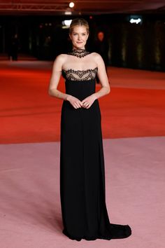 a woman standing on top of a pink carpet wearing a long black dress with lace at the neck