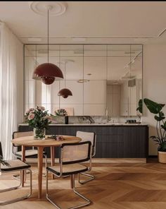 a dining room table and chairs in front of a large mirror with plants on it