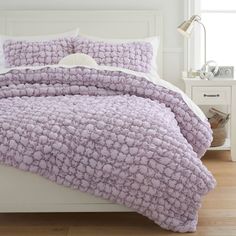 a bed with a purple comforter and pillows