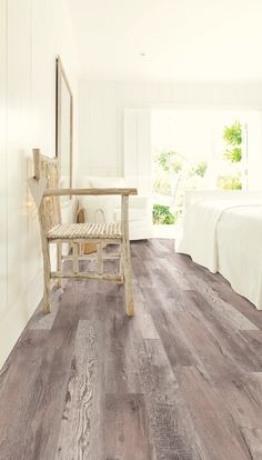 a bedroom with white walls and wood floors, two beds in the background and a chair on the floor