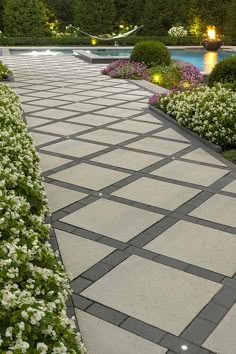 the walkway is lined with white flowers and greenery next to a swimming pool at night