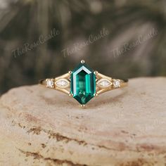 an emerald and diamond ring sitting on top of a rock