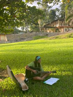 a man sitting in the grass playing an acoustic guitar and paper on his lap top