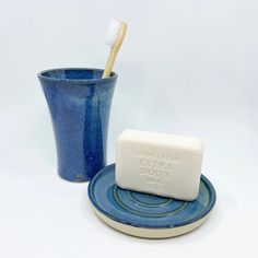 a blue cup with a toothbrush in it next to a soap bar on a plate