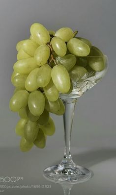 a glass filled with green grapes sitting on top of a table