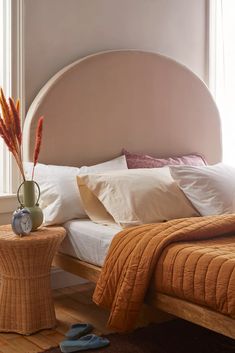 a bed sitting next to a window covered in pillows and blankets on top of a wooden floor