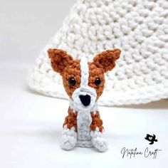 a small brown and white dog sitting next to a crocheted hat