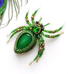 a green spider brooch sitting on top of a white table next to a peacock feather