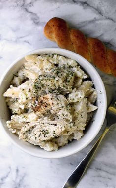 a white bowl filled with pasta next to a piece of bread on top of a table