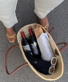 a person standing next to a basket filled with wine bottles and other items on the ground