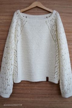 a white crocheted sweater hanging on a wooden hanger