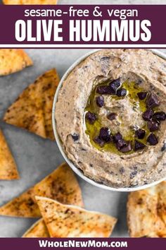 hummus with olives in a white bowl surrounded by tortilla chips