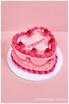 a pink heart shaped cake with cherries on top and the word love spelled in large letters