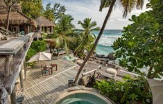 an outdoor hot tub sitting on top of a wooden deck next to the ocean and palm trees