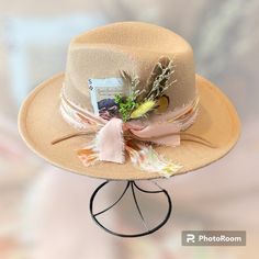 The Bentley is ready for that concert or church. It has a pink base with a twisted tie dye chiffon wrapped around and tied. Then it is double wrapped in tan leather.  Tucked behind the band is a few feathers and flowers.  Then tied together with a burnt edged card displaying The Great Sand Dunes.  So elegant but edgy.   This hat is tan and fedora style.  Head circumference is 56-58 cm and can be adjusted on the inside with a tie.  The brim measures 2.95 inches and made of 65% cotton and 35% polyester.   Each hat from The Bandit Hat Co has been customized with my own personal touch.  Each hat that has been created is unique and there will never be two the same. Adjustable Hat Bands For Country Events In Spring, Western Style Adjustable Fedora For Spring, Adjustable Felt Hat For Country Summer Events, Adjustable Felt Hat For Summer Country Events, Spring Western Style Adjustable Fedora, Spring Western Fedora With Adjustable Fit, Adjustable Summer Felt Hat For Country Events, Adjustable Felt Hat For Summer Party, Spring Church Hats With Brim