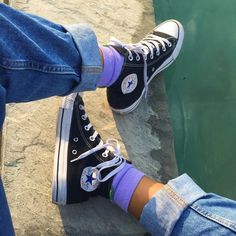 two people wearing black and purple converse shoes by the water with their feet propped up