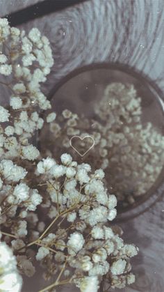 a bouquet of white flowers with a heart shaped ring on the center and behind it is a wooden table