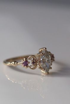 a close up of a ring with an oval shaped diamond and two small pink stones