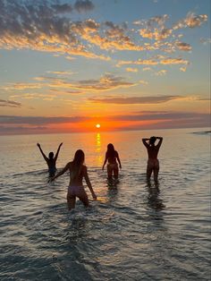 three girls in the water at sunset with their arms up and hands behind their heads