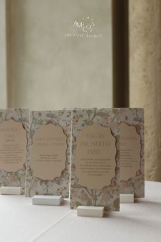 three cards are sitting on top of a table with white linens and floral designs