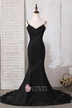 a black evening gown with straps and laces on the bottom, in front of a white wall