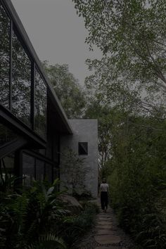 a person walking down a path in front of a building with trees and bushes on both sides