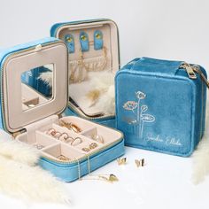 an open blue suitcase with jewelry in it on a white surface next to other items