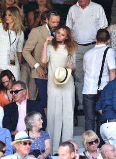 a woman wearing a white dress and hat standing in front of a crowd