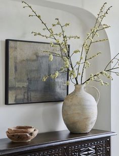 a vase with white flowers sitting on top of a wooden table next to a painting