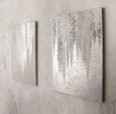 two silver paintings hanging on the wall next to each other