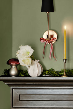 a mantle with flowers, candles and other items on it in front of a green wall