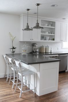 a kitchen with white cabinets and gray counter tops, along with bar stools that match the hardwood flooring