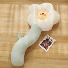 a white flower shaped pillow sitting on top of a wooden floor next to a magazine