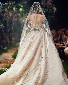 the back of a wedding dress on display at a fashion show with people in the background