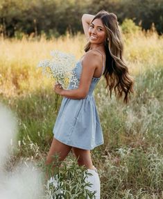 a beautiful young woman walking through a field holding a bouquet of flowers in her hand