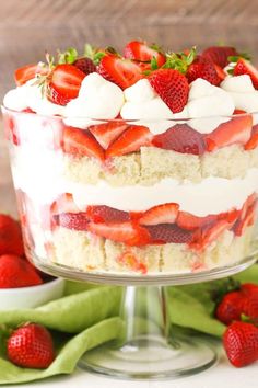 a layered cake with strawberries on top and whipped cream in the middle, sitting on a glass pedestal