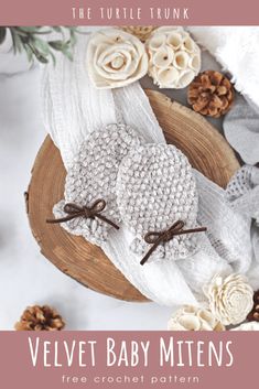 two knitted mittens sitting on top of a wooden plate next to pine cones and flowers