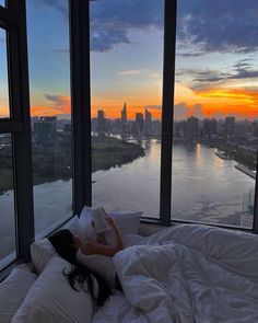 a person laying on a bed in front of large windows overlooking the city at sunset