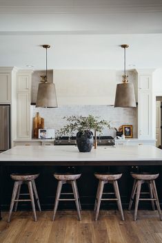 a large kitchen island with stools in front of it and lights hanging from the ceiling