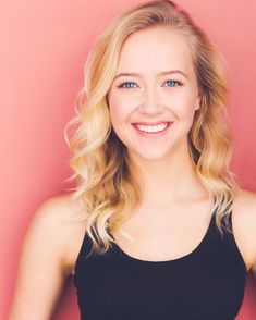 a woman with blonde hair and blue eyes smiles at the camera while wearing a black tank top