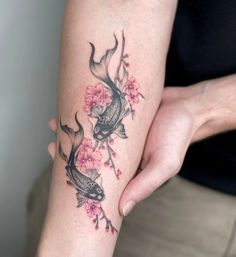 a woman with a tattoo on her arm holding a fish and cherry blossom tree branch