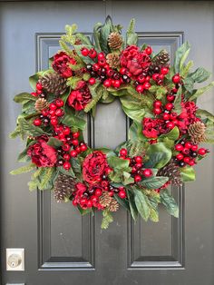 a wreath with red berries, pine cones and green leaves is hanging on the front door