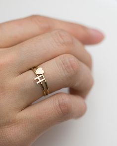 a woman's hand wearing a gold ring with a small heart on the middle