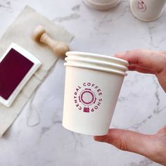 a person holding a coffee cup in their hand next to some other items on the table