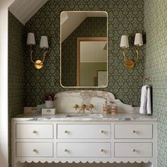 a bathroom with green and white wallpaper, gold fixtures and a large mirror above the sink