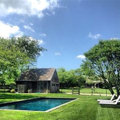 an empty swimming pool in the middle of a grassy area with lawn chairs and trees