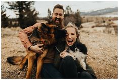 a man and woman are sitting on the ground with their two german shepherd puppies