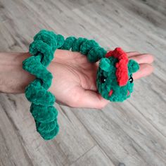 a hand holding a green toy with a red hat on it